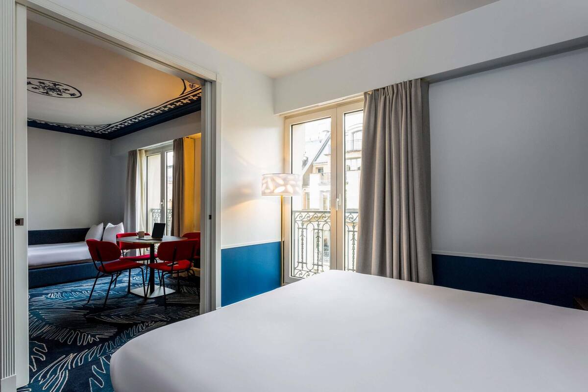 A hotel room with a bed, a desk with a chair, a sofa, and a window with curtains.