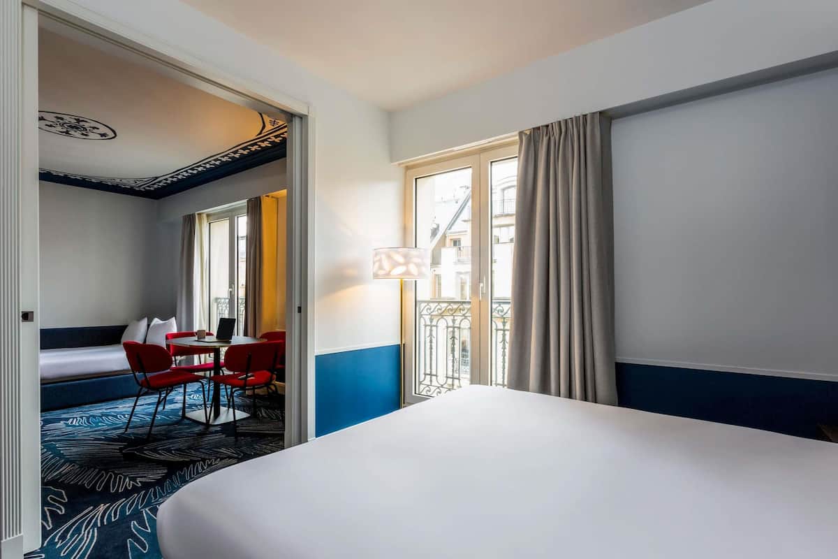 A hotel room with a bed, a desk with a chair, a sofa, and a window with curtains.
