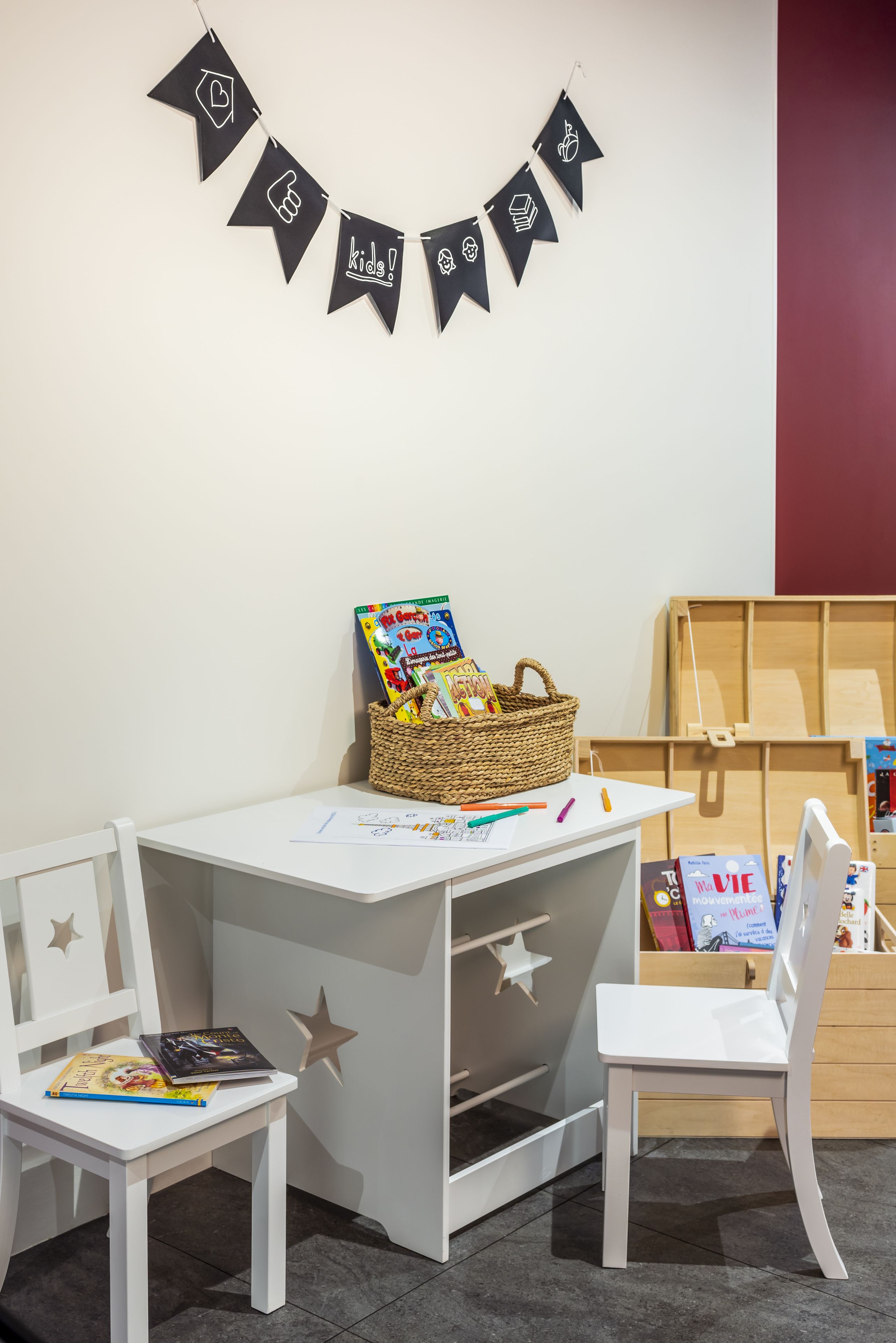 Un espace de jeux pour enfants avec un bureau blanc, deux chaises blanches, une décoration murale en forme d’étoile et un panier rempli de jouets.
