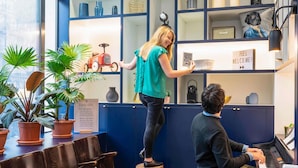 A person standing on a stool in a room with a piano, shelves with decorative items, and potted plants. - Aparthotel Adagio Paris Haussmann (Paris)
