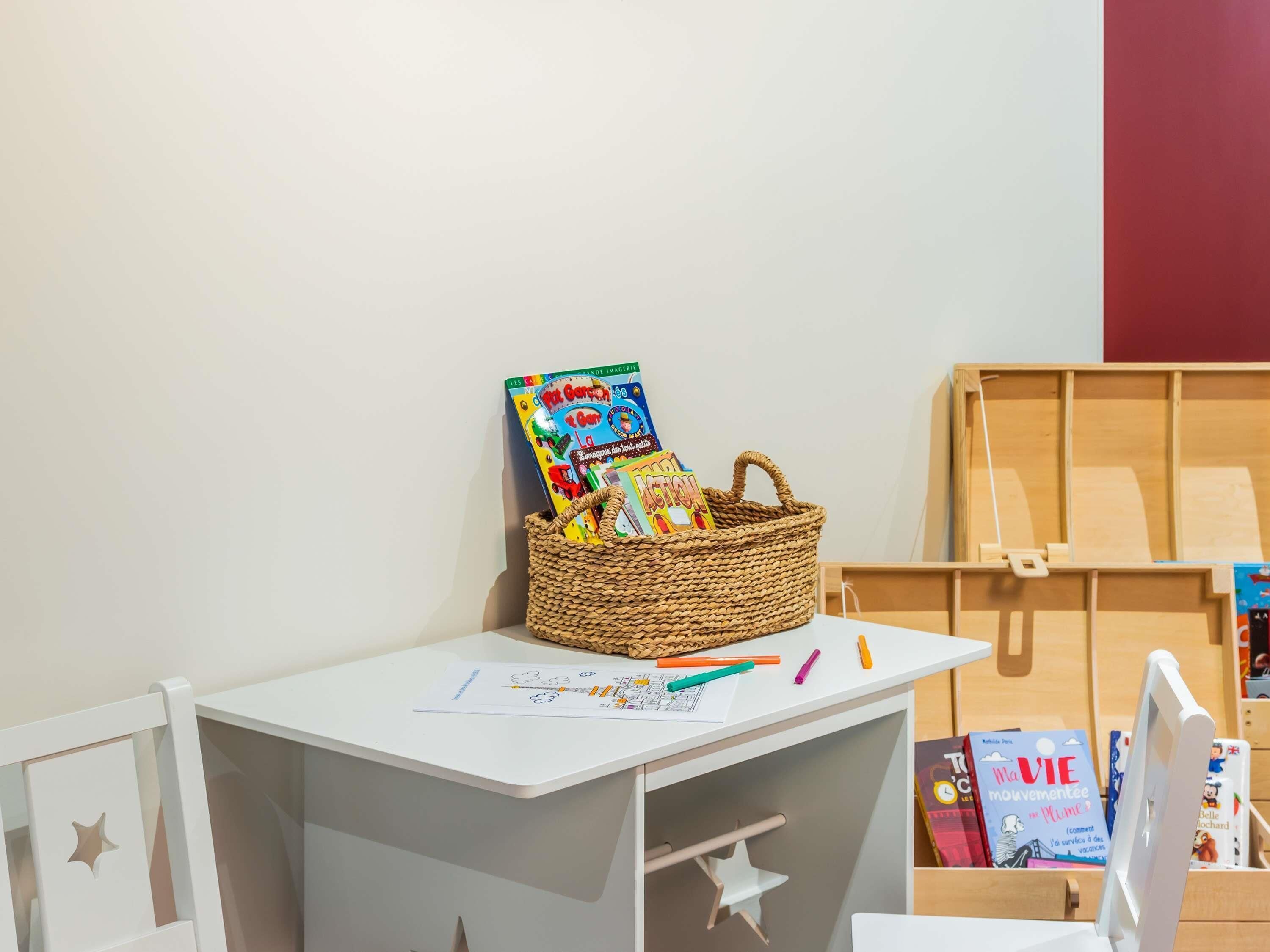 A child's play area with a white table, a woven basket with books, and a wooden play structure.