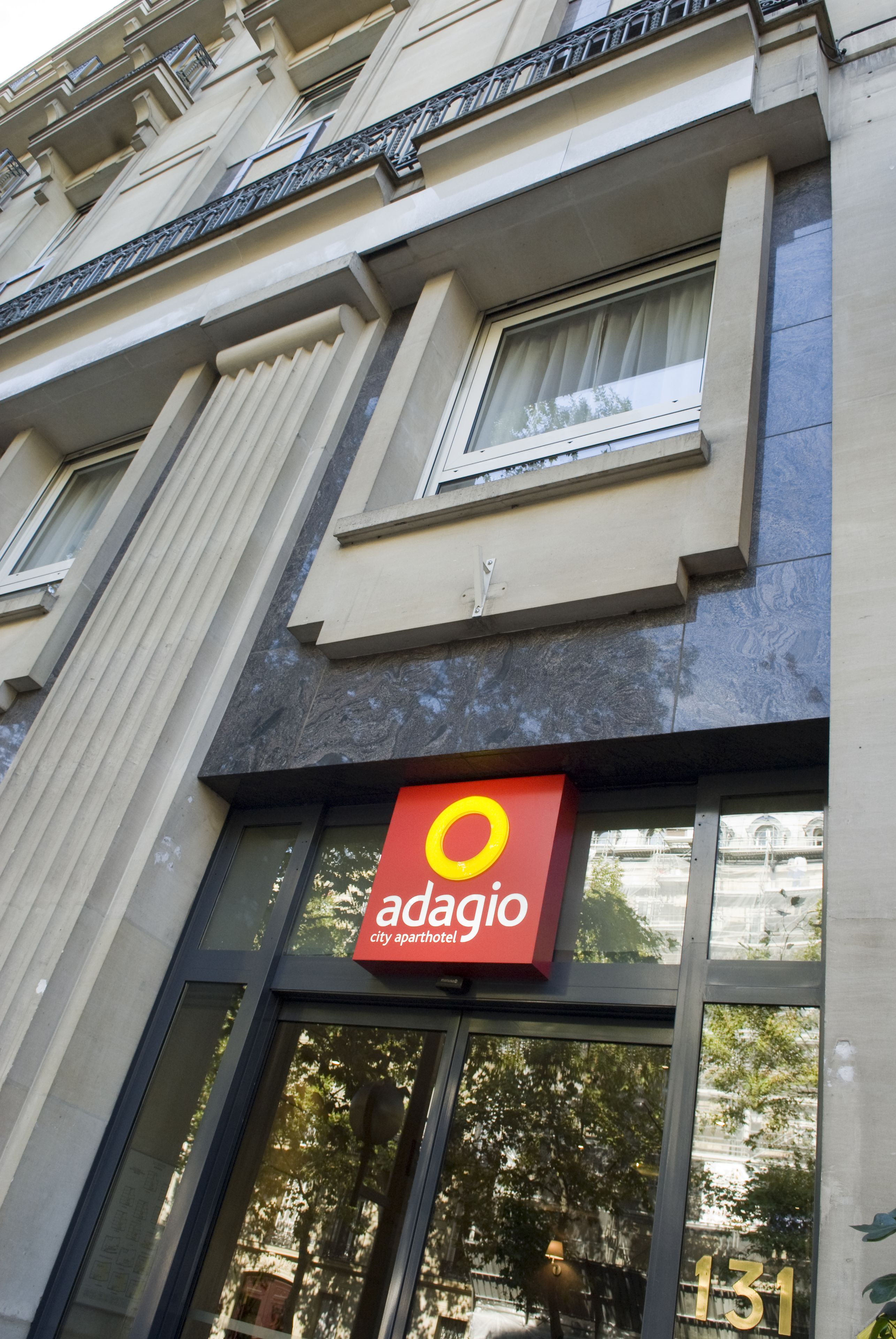 Un immeuble avec une enseigne indiquant « Adagio City Aparthotel » et le numéro « 131 » sur la fenêtre.