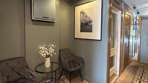 A hallway with a checkered floor, a framed picture on the wall, a vase with flowers, and a sofa. - Garden View Hotel (London)