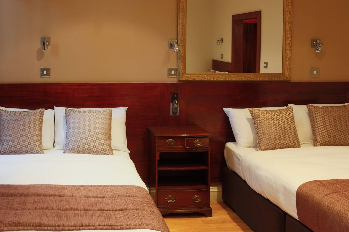 A hotel room with two beds, a nightstand, a mirror, and a wooden headboard.
