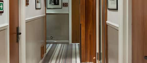Ein Hotelgang mit Streifenmuster-Teppich, Holzvertäfelung und gerahmten Bildern an der Wand.