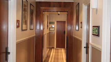 A hotel hallway with wooden doors, framed pictures, a striped carpet, and recessed lighting.