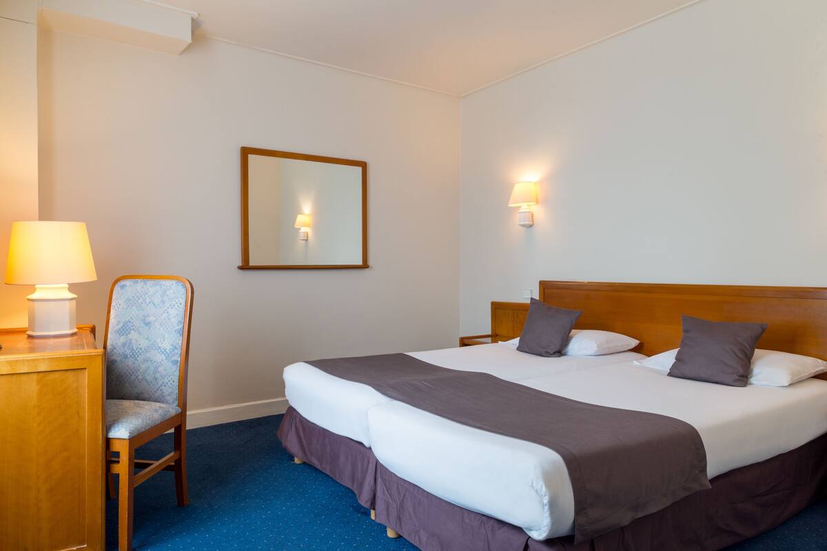A hotel room with a bed, a chair, a lamp, and a wall-mounted mirror.