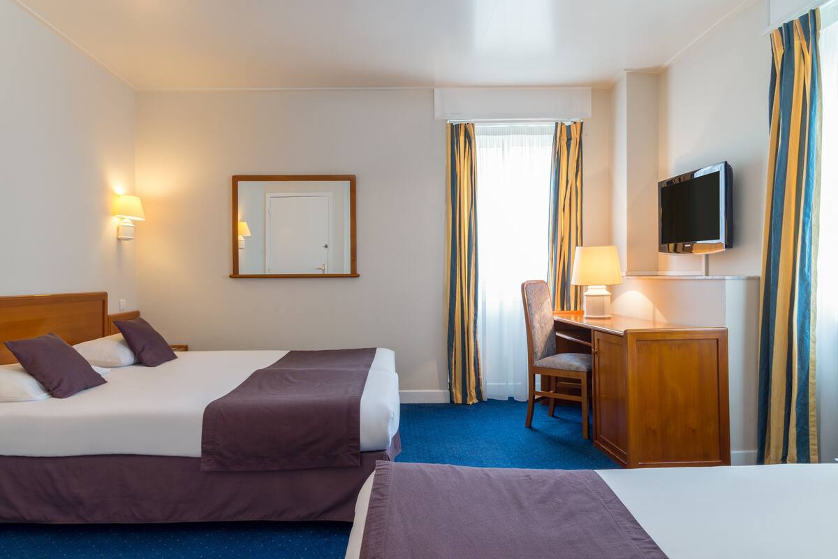 A hotel room with two beds, a desk, a chair, a television, and a window with curtains.