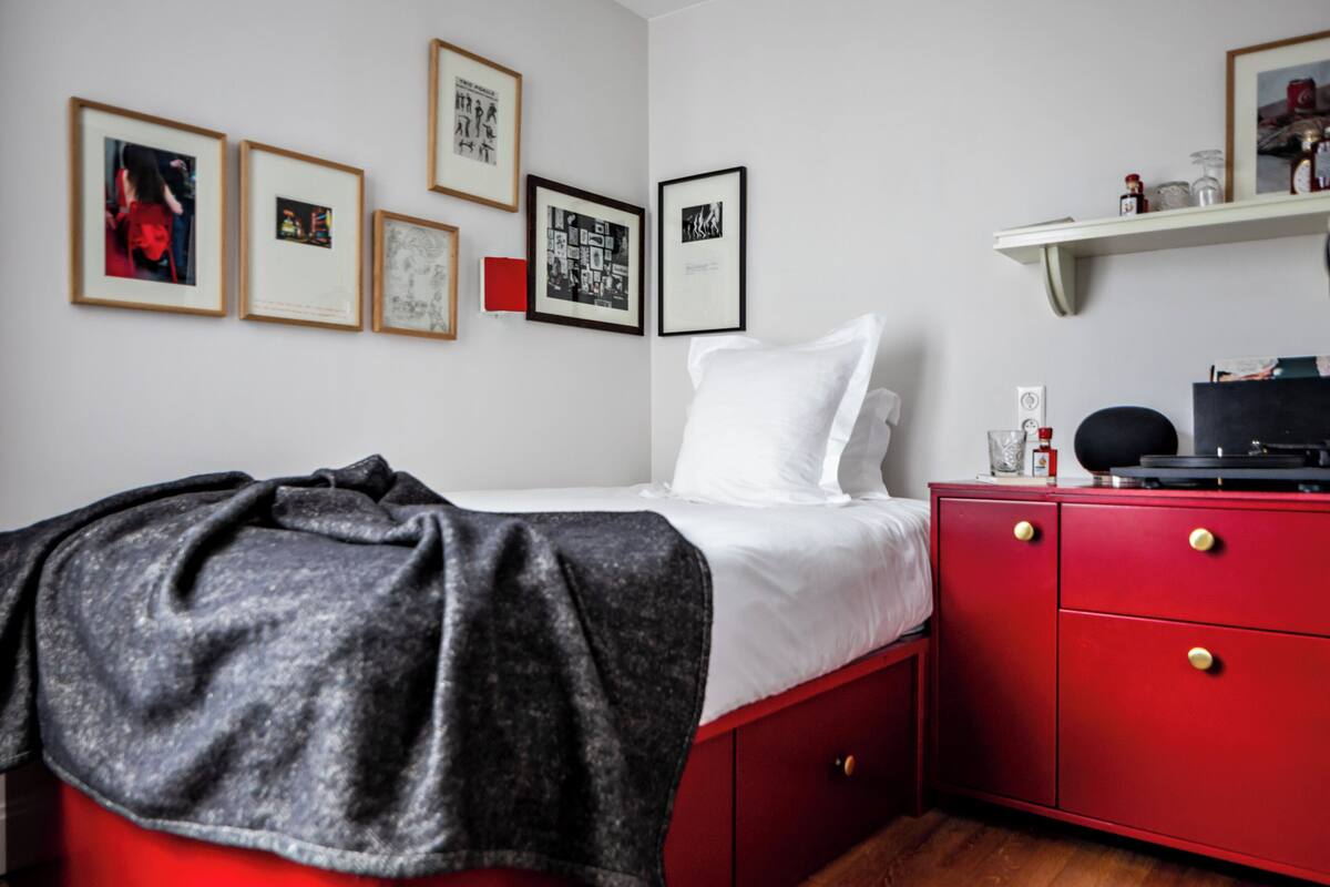 A bedroom with a bed, a red dresser, and framed pictures on the wall.