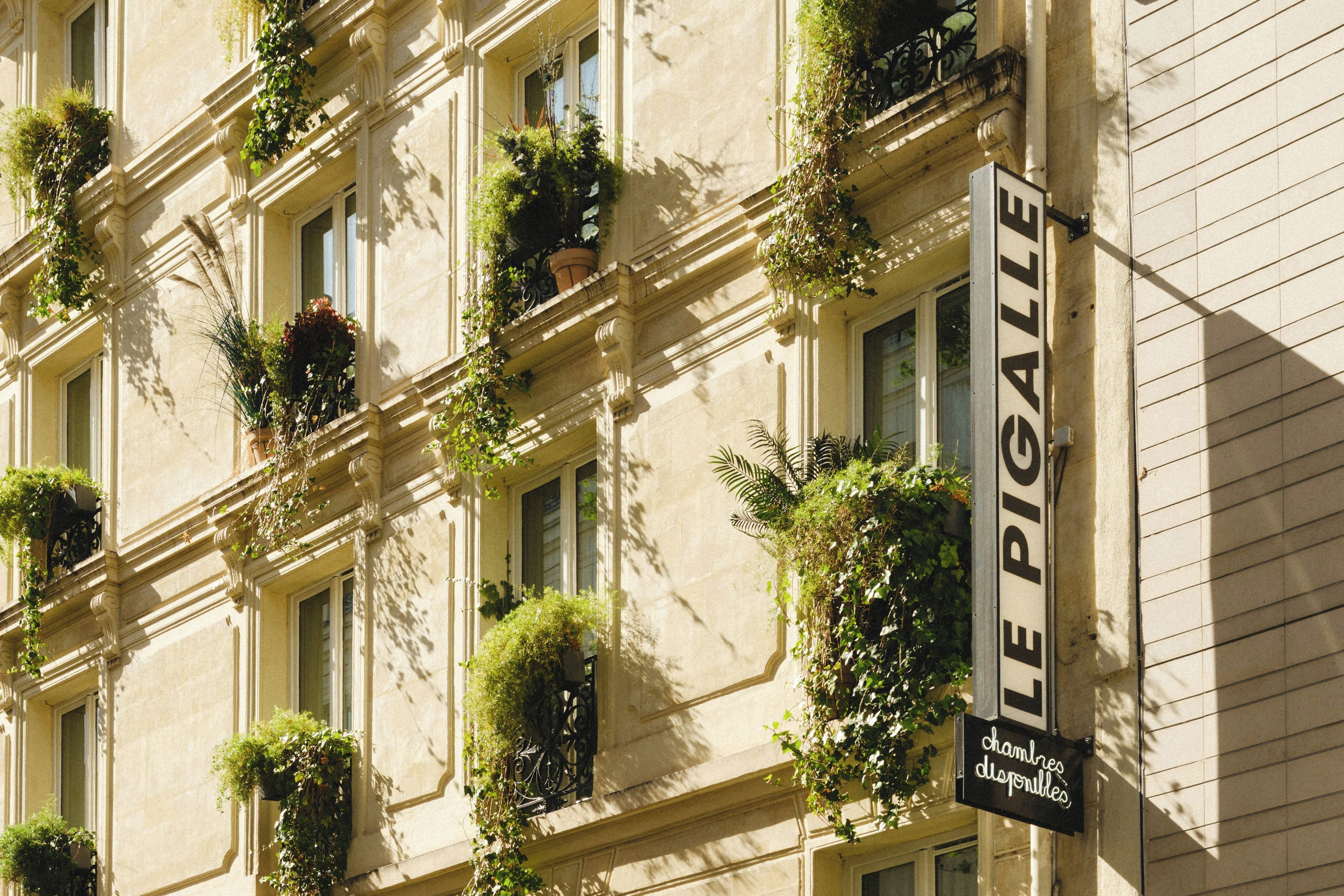 A building facade with multiple windows, some with plants. A sign reads 'LE PIGALLE' with additional text 'chambres disponibles' indicating available rooms.