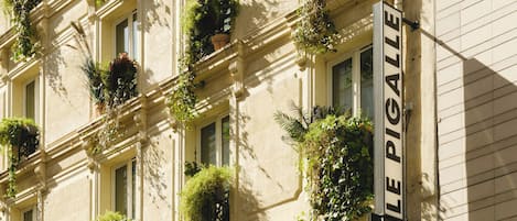 A building facade with multiple windows, some with plants. A sign reads 'LE PIGALLE' with additional text 'chambres disponibles' indicating available rooms.