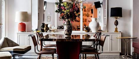 Un comedor con una mesa redonda, sillas, un jarrón con flores y una base roja.