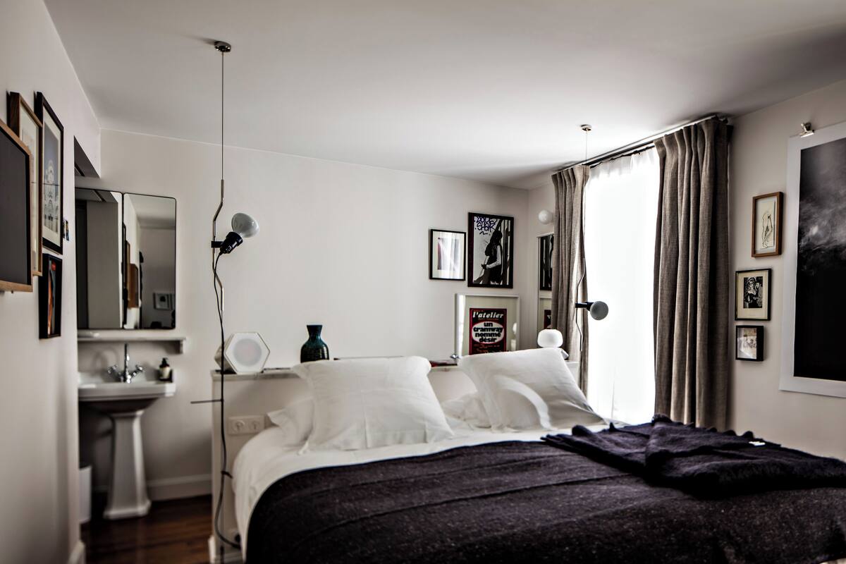A modern bedroom with a bed, bedside table, lamp, and a large window with curtains.