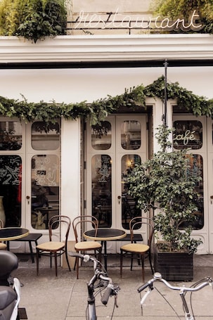 A cafe with outdoor seating, a sign above the entrance, and a potted plant in the foreground.