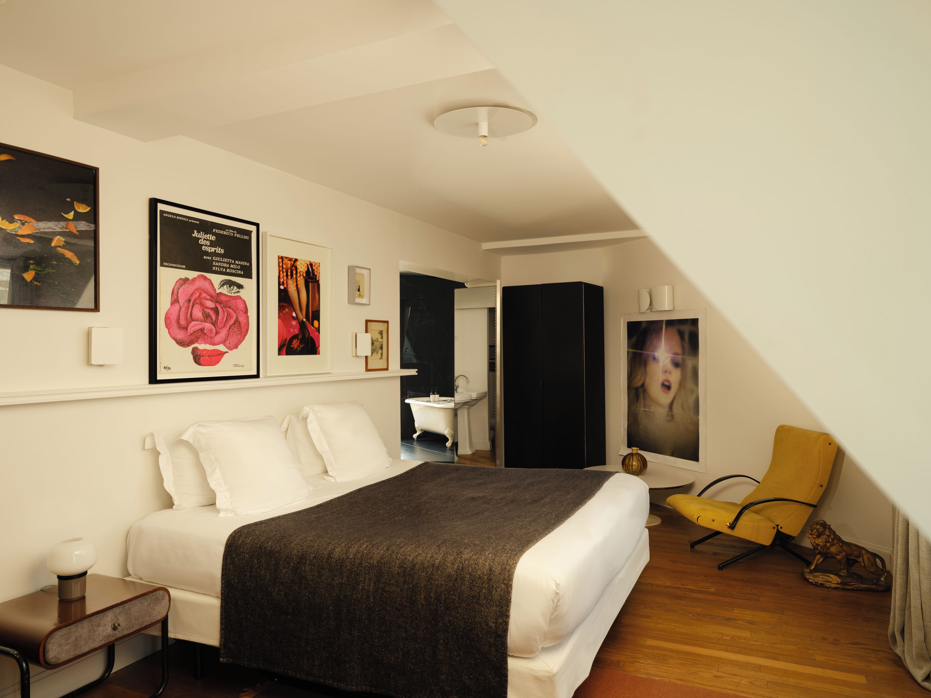 Un dormitorio con cama, mesita de noche, una silla, armario y una obra de arte en la pared.