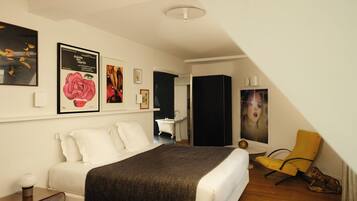 A bedroom with a bed, a bedside table, a chair, a wardrobe, and artwork on the wall.