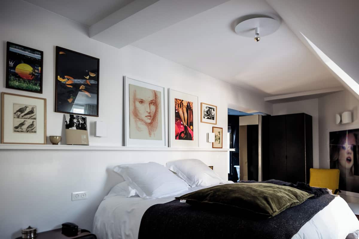 Un dormitorio con cama, paredes blancas y varias obras de arte enmarcadas.