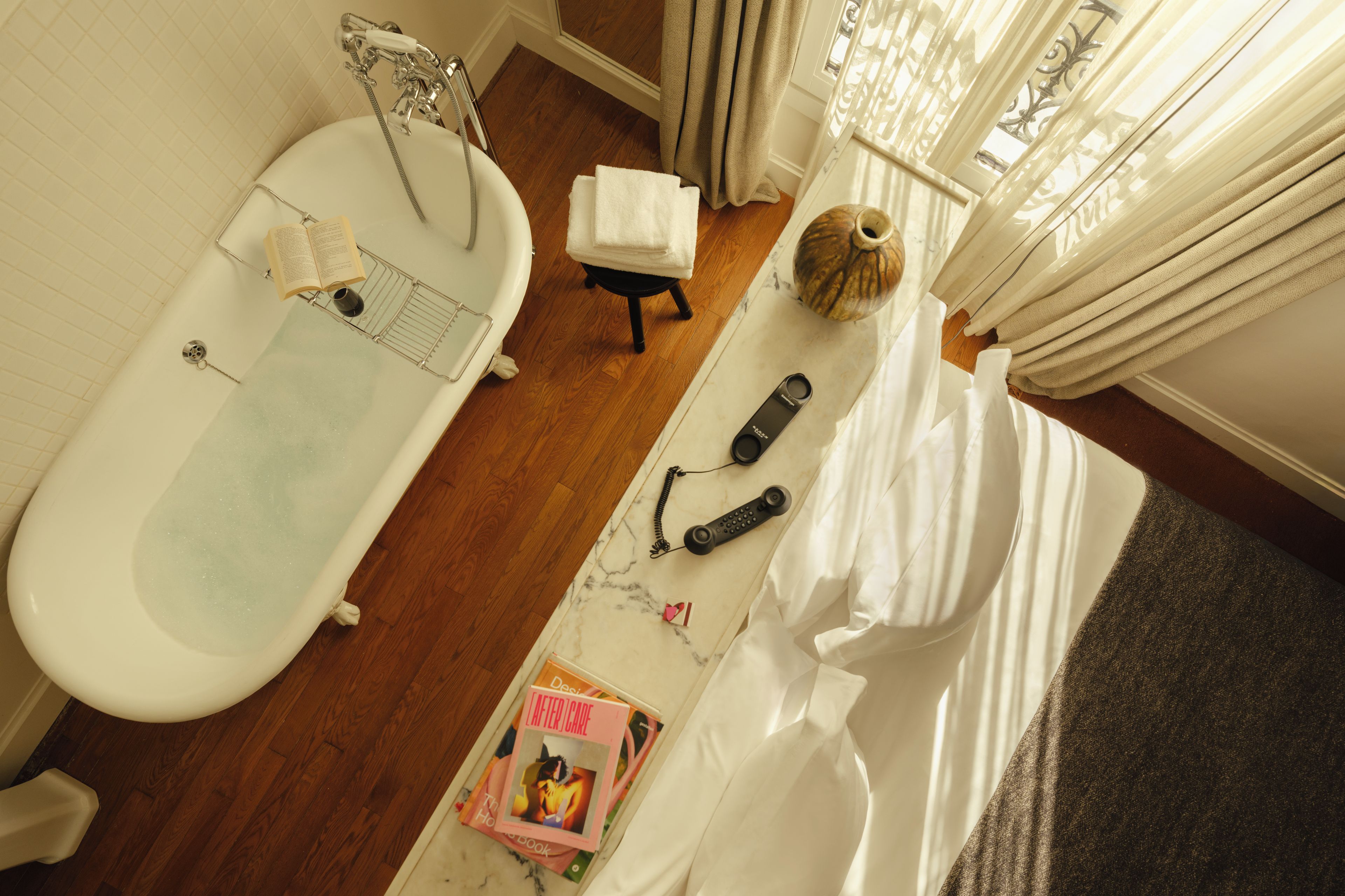 A bathroom with a bathtub, a shower, a towel, a book, a remote control, and a decorative vase.