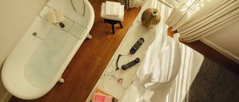 A bathroom with a bathtub, a shower, a towel, a book, a remote control, and a decorative vase.