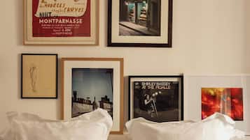 Un lit avec des oreillers blancs, une affiche encadrée représentant un personnage de dessin animé et plusieurs photographies encadrées accrochées au mur.