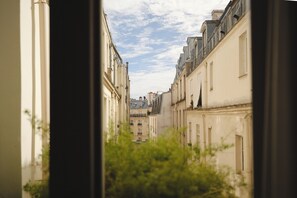 A narrow street with buildings on either side, viewed through a window with greenery in the foreground. - Le Pigalle, a Member of Design Hotels (Paris)