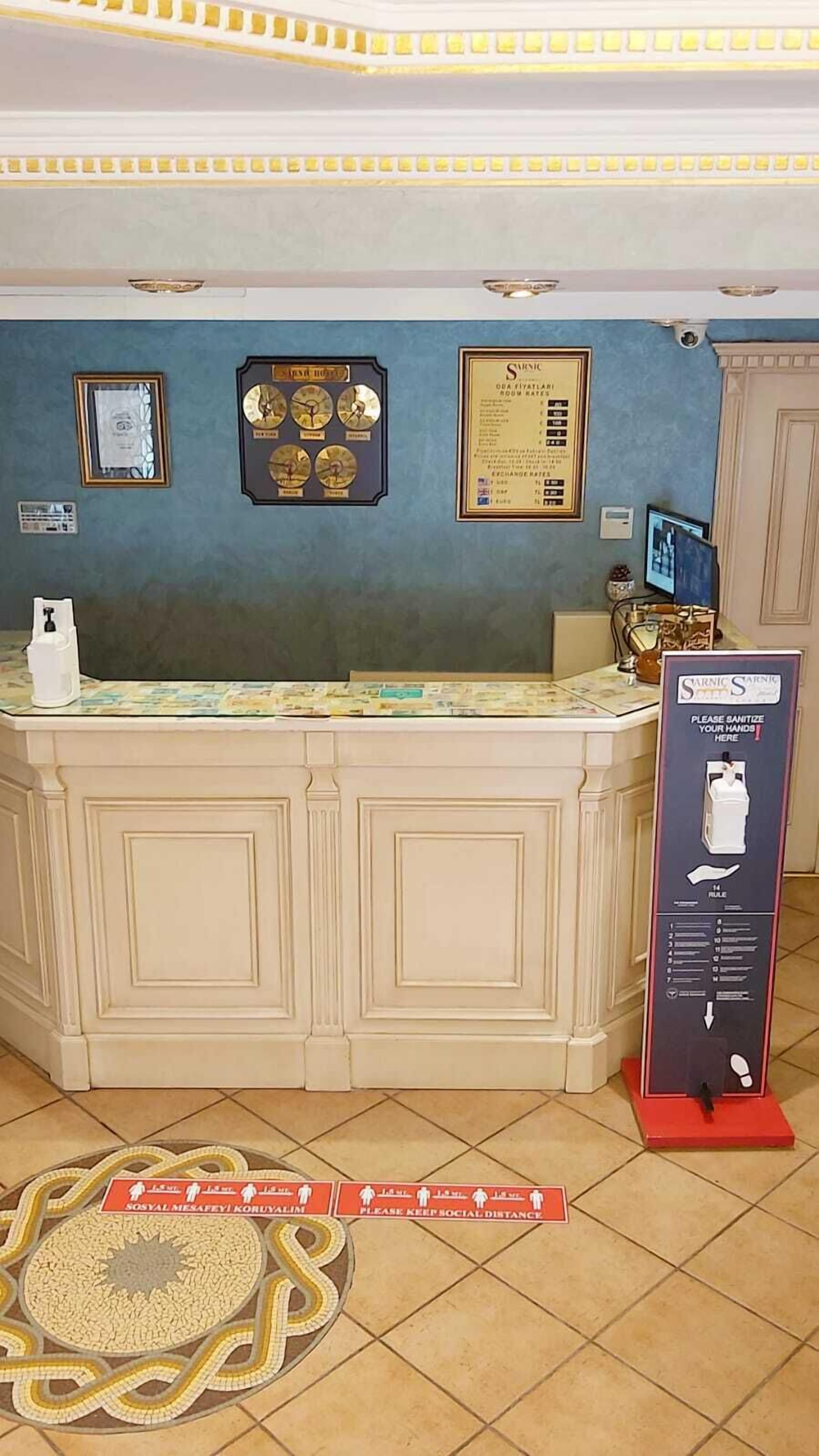 Una zona reception con un bancone, certificati incorniciati, un orologio e un distributore di gel igienizzante.