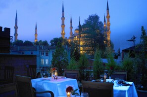 An outdoor dining area with tables set for two, surrounded by trees and buildings.