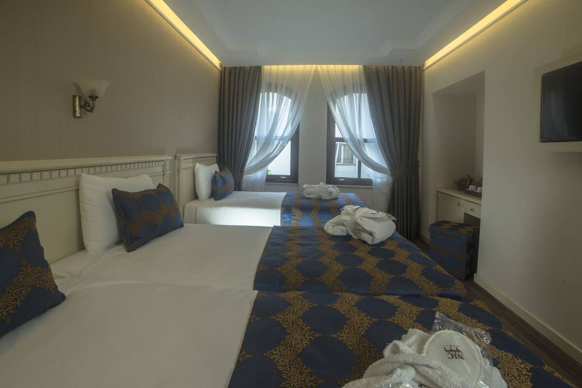 A hotel room with two beds, a TV, a desk, and a window with curtains.