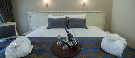 Une chambre d’hôtel avec un lit, deux lampes fixées au mur, un plateau avec une bouteille et des verres, et deux serviettes sur le lit.