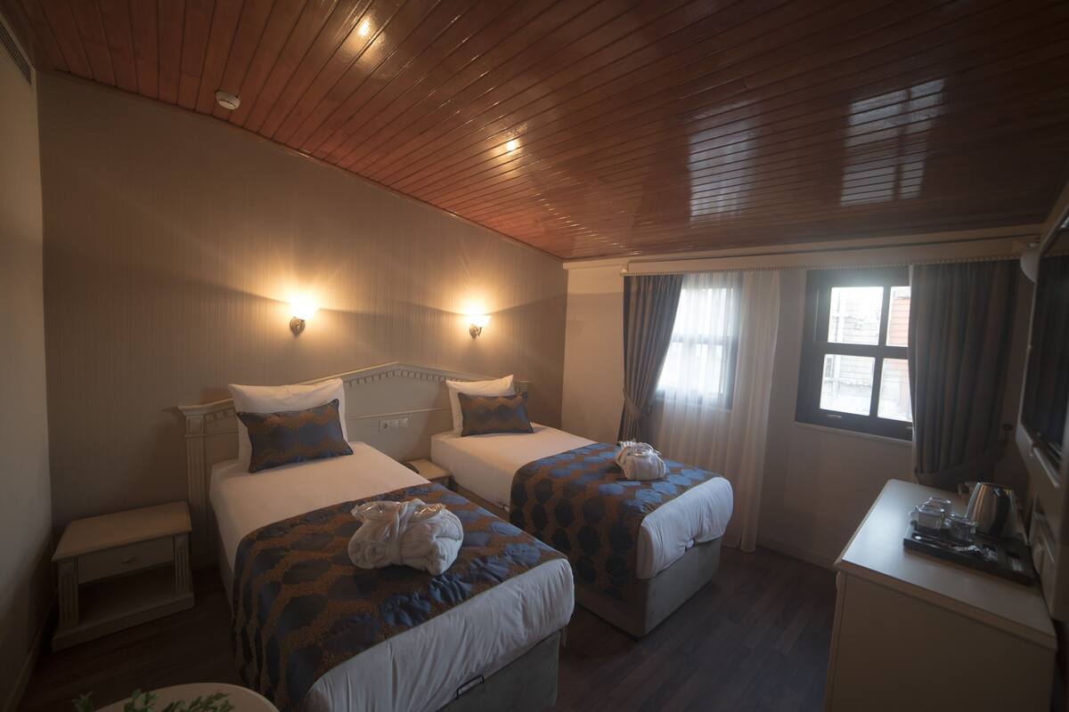 A hotel room with two beds, a desk, and a window with curtains.