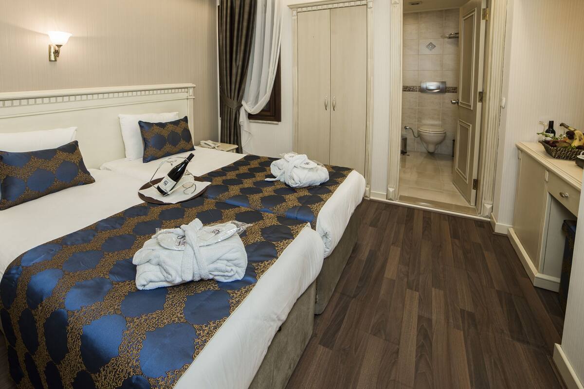 A hotel room with a large bed, a nightstand, a bathroom with a shower and toilet, and a vanity with a mirror.