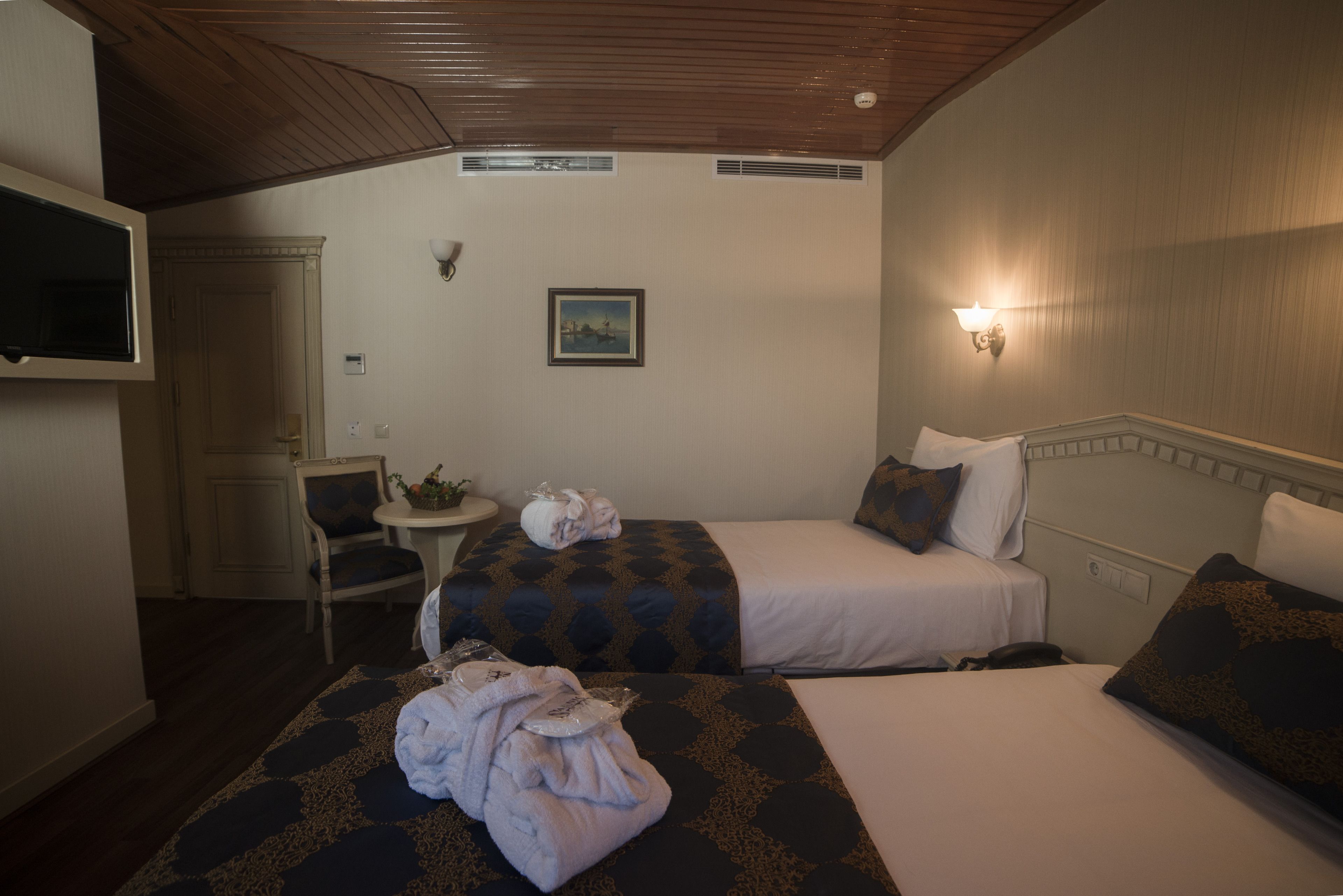 Une chambre d’hôtel avec deux lits, une chaise, une petite table, un t éléviseur et un tableau au mur.