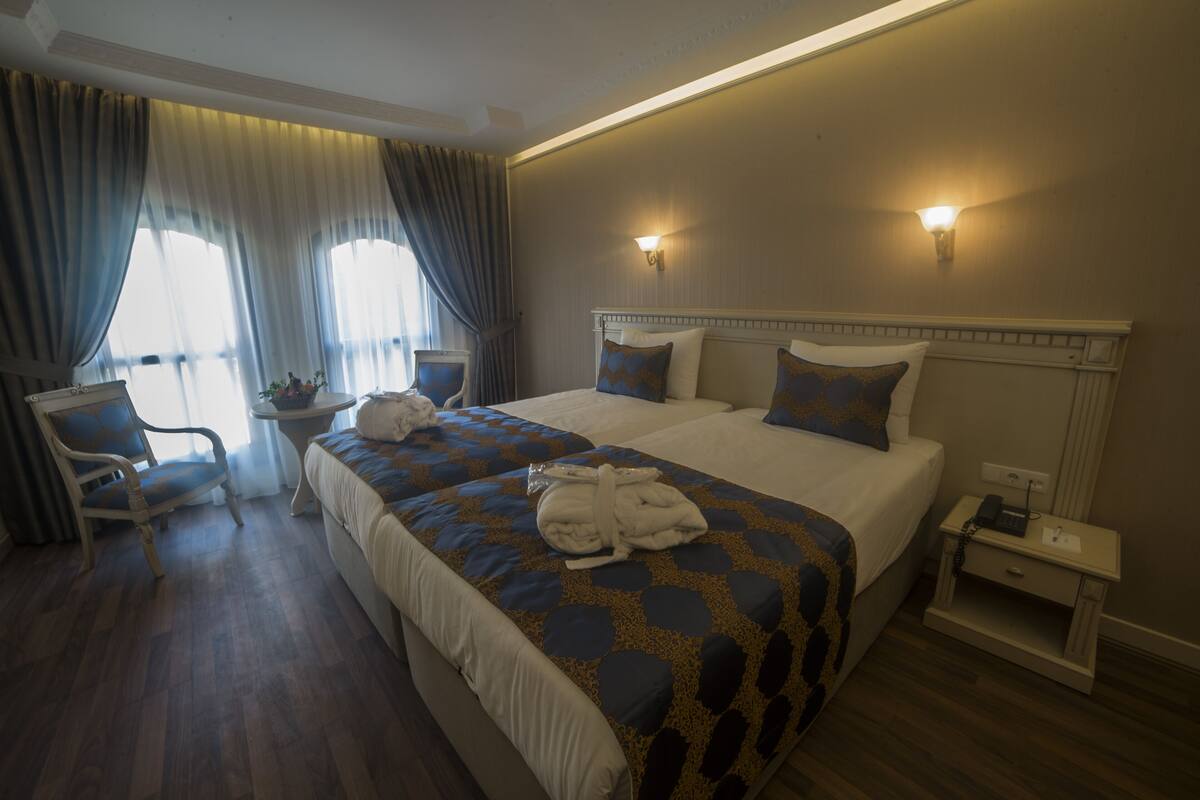A hotel room with two beds, a chair, a nightstand with a phone, and a window with curtains.