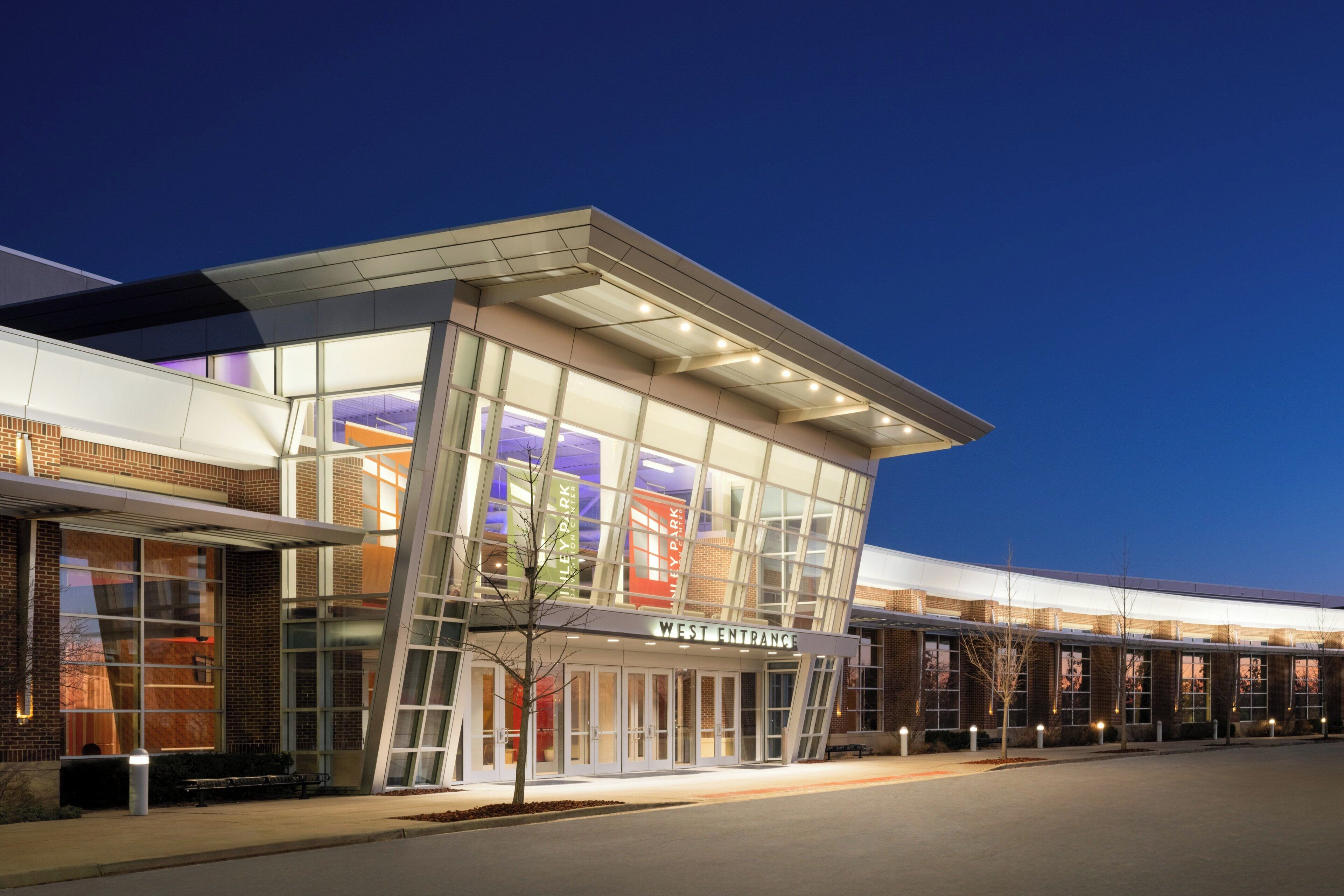 A modern building with a glass facade, a prominent entrance labeled 'WEST ENTRANCE,' and a series of windows and doors.