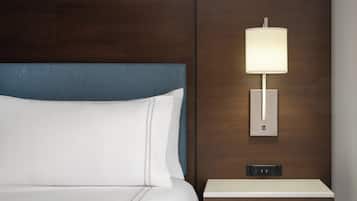 Quarto de hotel com cama, mesa de cabeceira com abajur e tomada na parede.