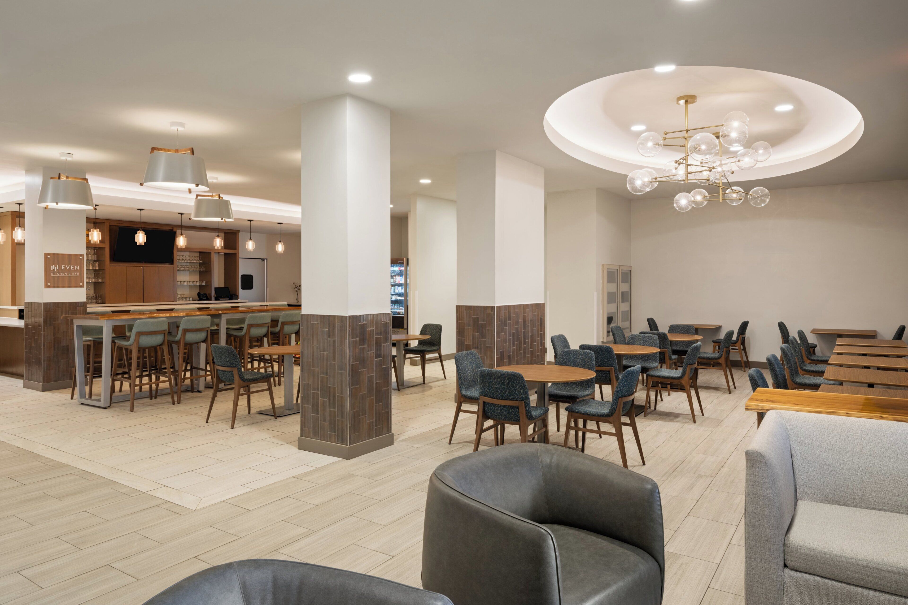 Un moderno vestíbulo de hotel con área de bar, disposición de asientos y una lámpara de techo original.