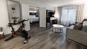 Habitación de hotel con cama, escritorio, sillón, televisión y bicicleta estática.