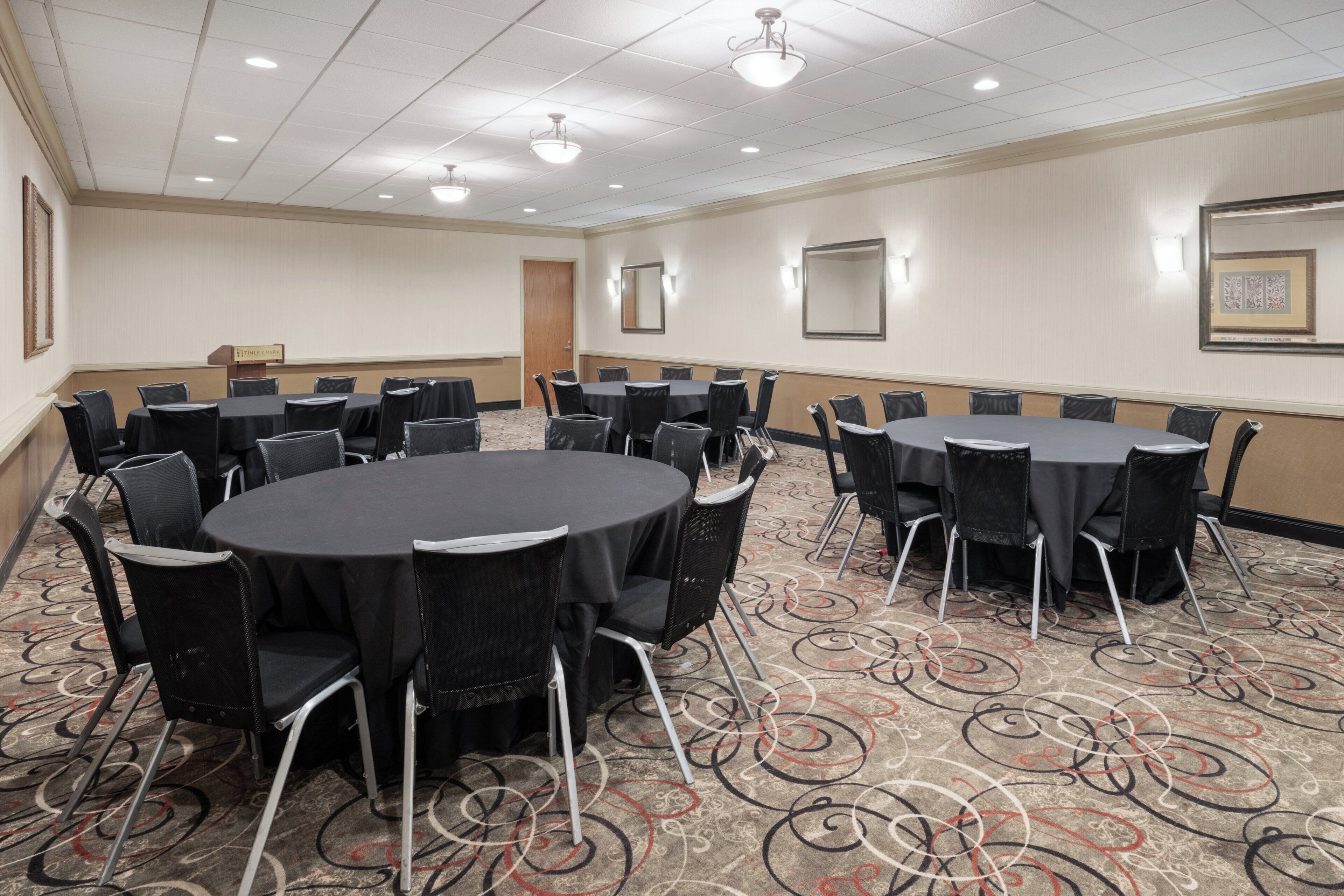 A conference room with round tables, black chairs, and a patterned carpet.