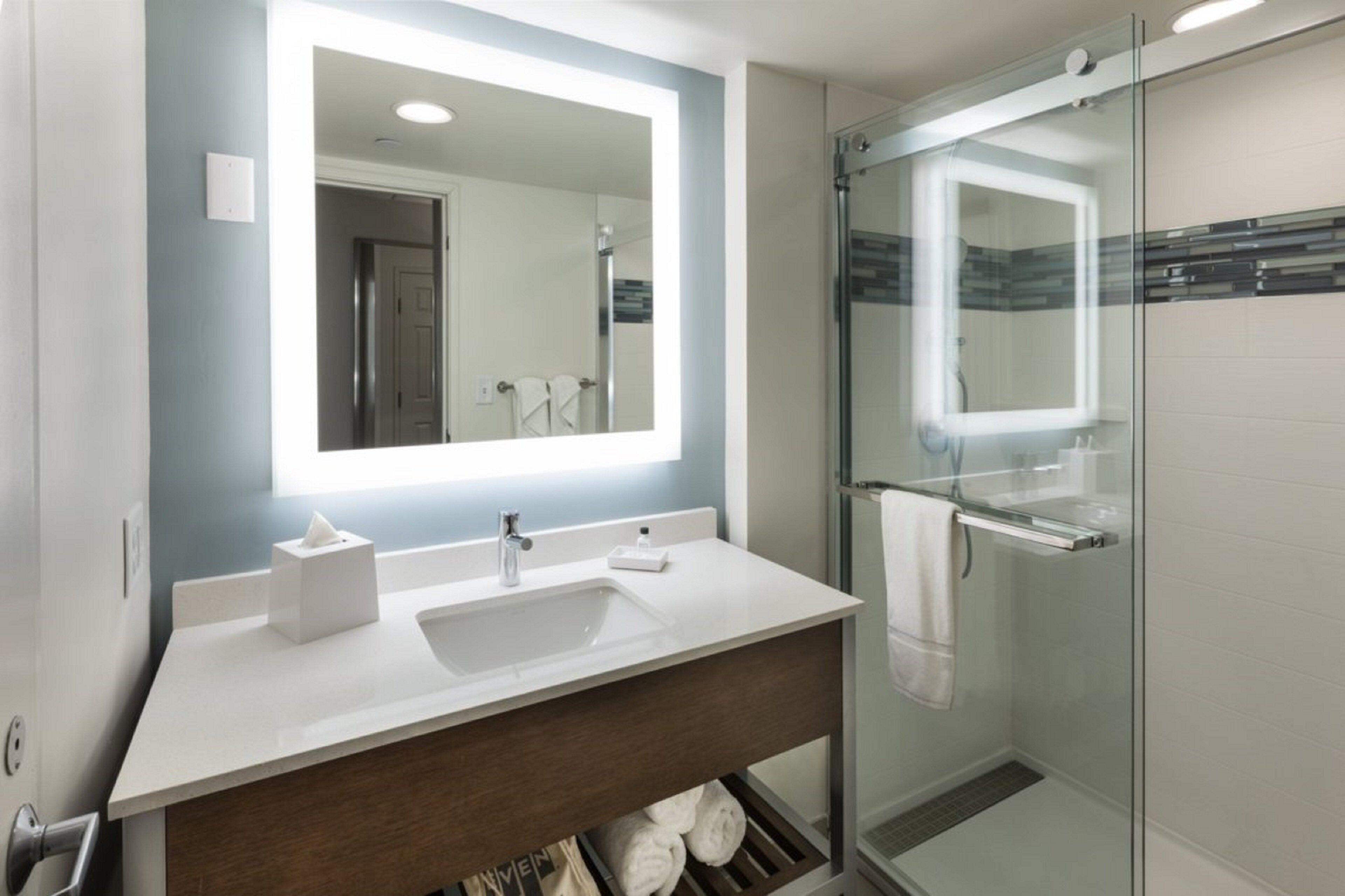 A modern bathroom with a large mirror, white sink, and glass shower enclosure.