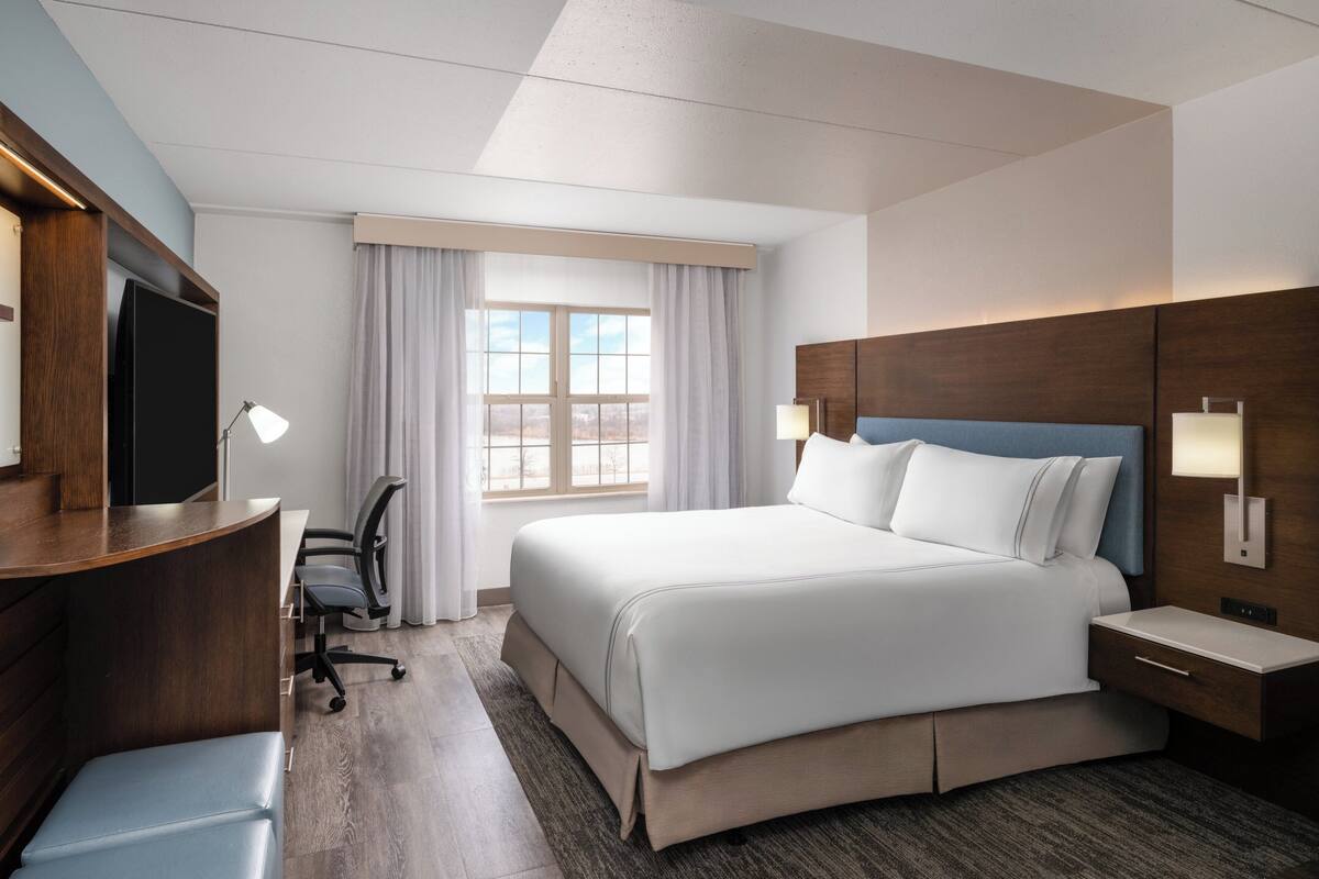 A hotel room with a bed, desk, chair, TV, and a window with curtains.