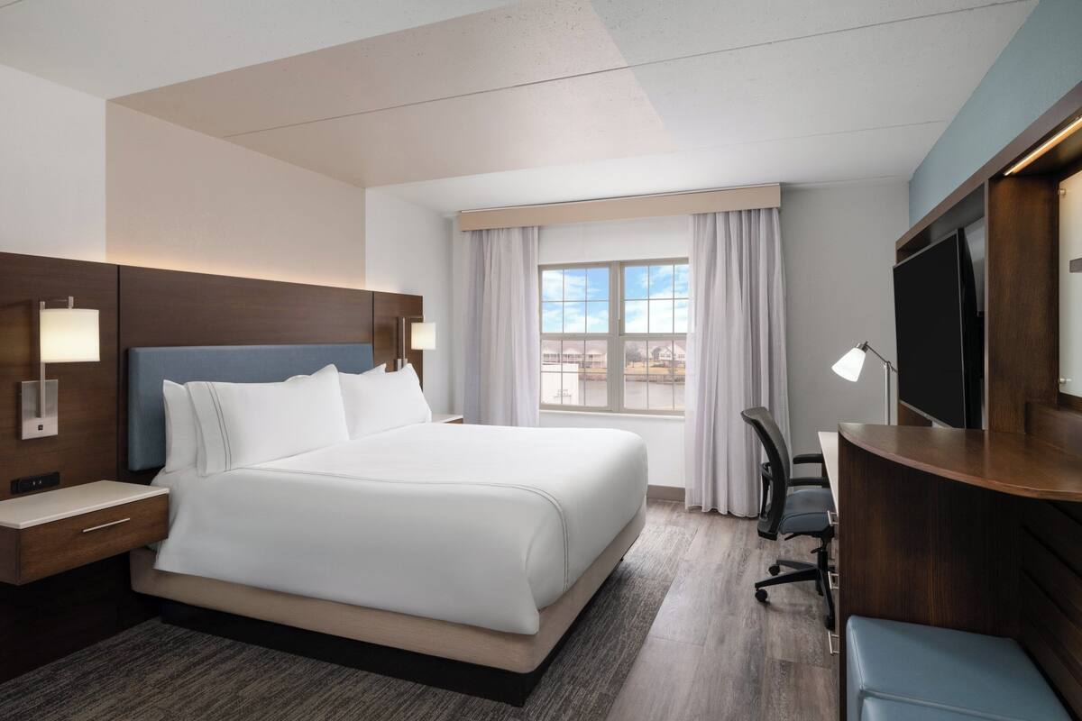 A hotel room with a large bed, a desk, a chair, a television, and a window with curtains.