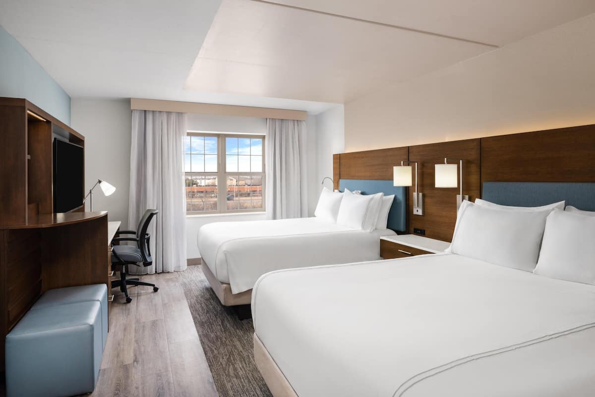 A hotel room with two beds, a desk with a chair, a television, and a window with curtains.