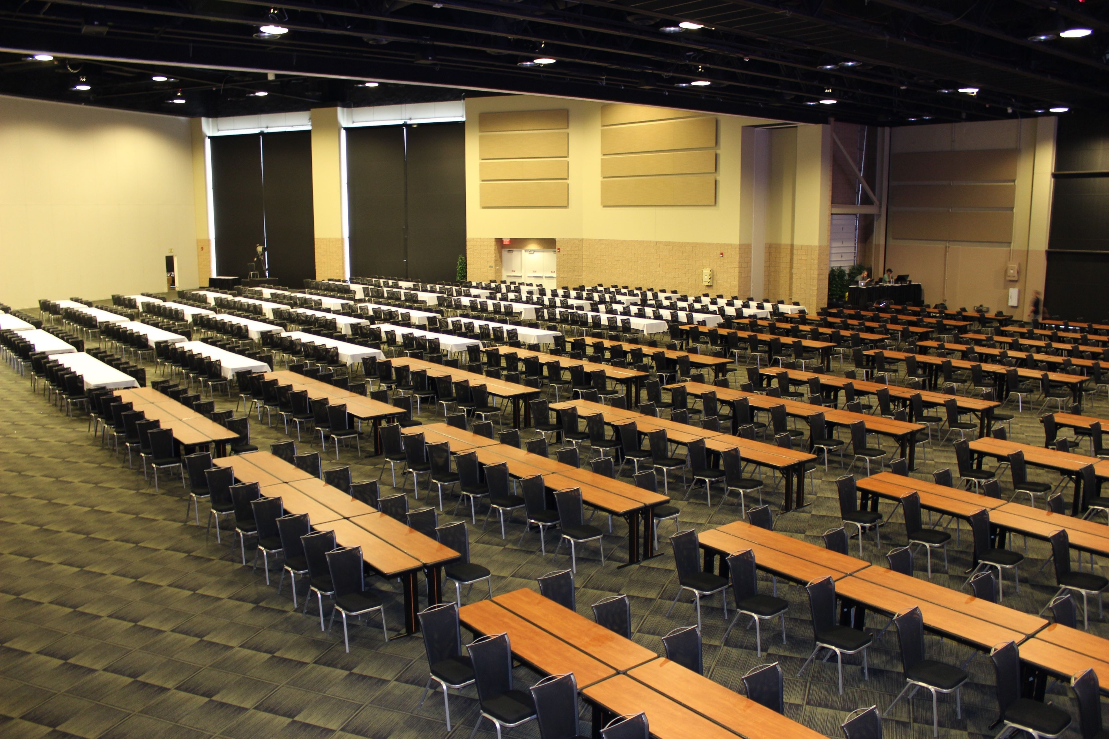 A large conference room with rows of tables and chairs, a stage, and a projector screen.
