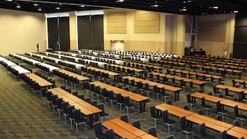 A large conference room with rows of tables and chairs, a stage, and a projector screen.