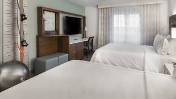 A hotel room with two beds, a desk, a television, exercise equipment, and a large window with curtains.