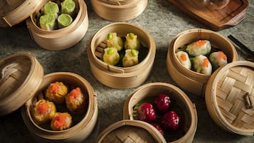 Verschiedene Dim-Sum-Gerichte in Bambusdämpfern, darunter grüne, gelbe und rote Teigtaschen sowie weitere gedämpfte Speisen.