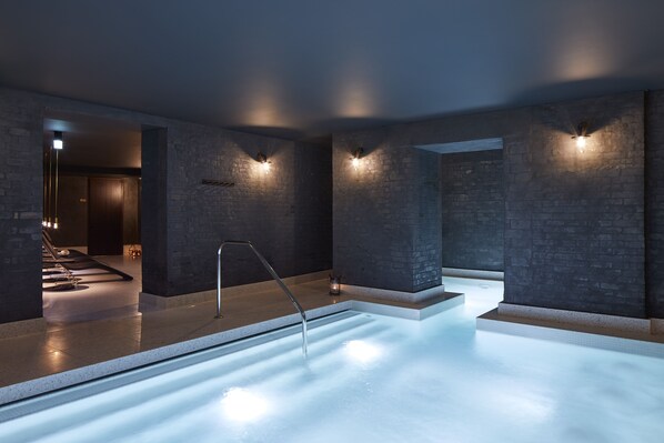 A modern spa with a heated pool, stone walls, and ambient lighting.