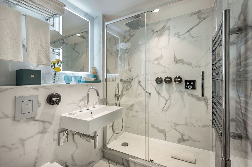A modern bathroom with a glass-enclosed shower, a white sink, and marble walls.