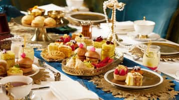 Una mesa adornada con diversos postres y pasteles, entre ellos tartas de frutas, bizcochos y cupcakes, dispuestos en bandejas y platos de oro labrado.