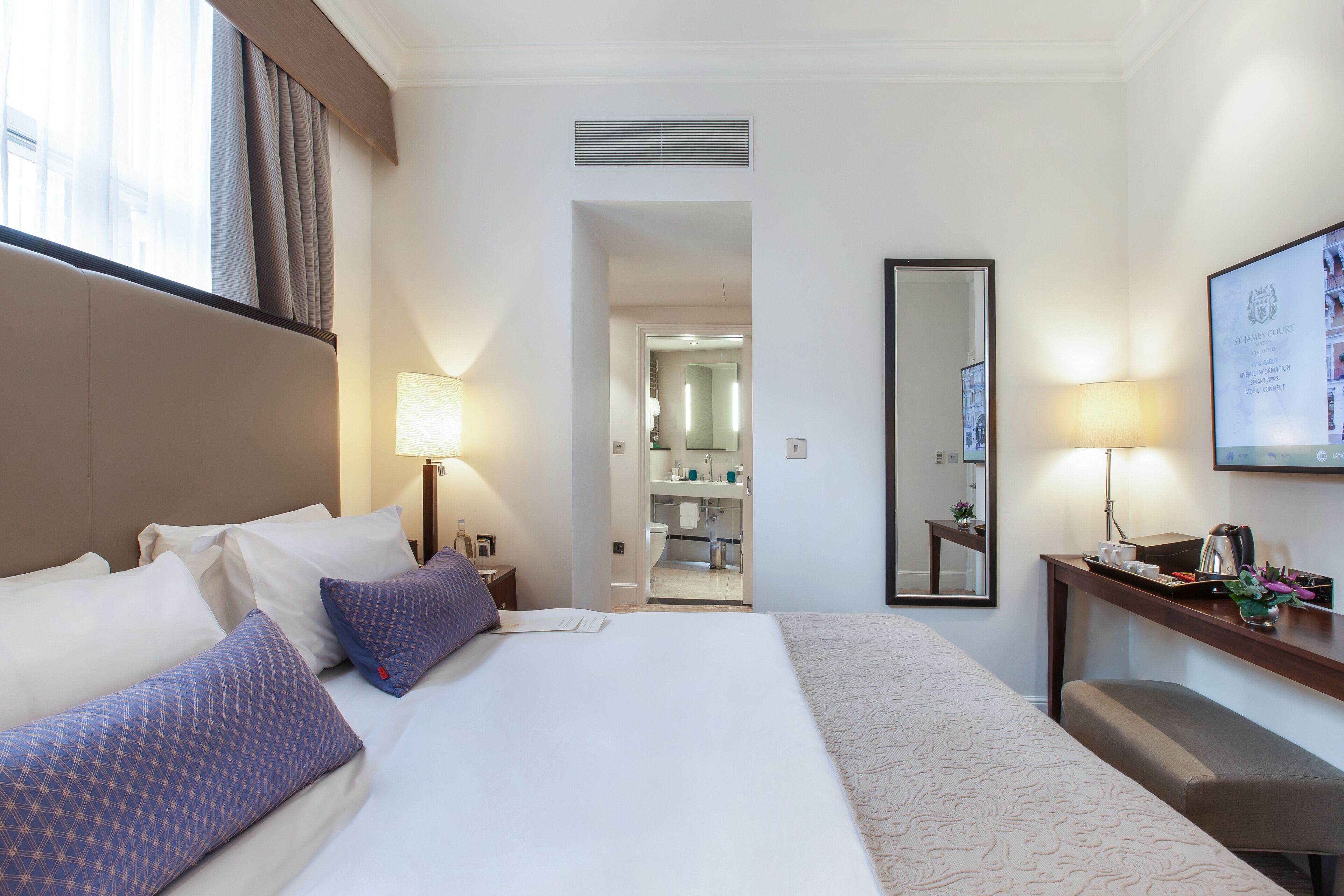 Habitación de hotel con una cama grande, un escritorio, un espejo y vistas al baño.